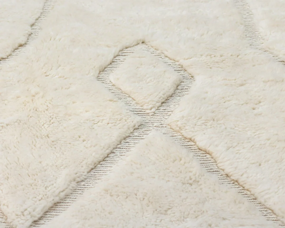 Close-up of a cream-colored, textured area rug featuring raised diamond patterns and subtle linear accents.