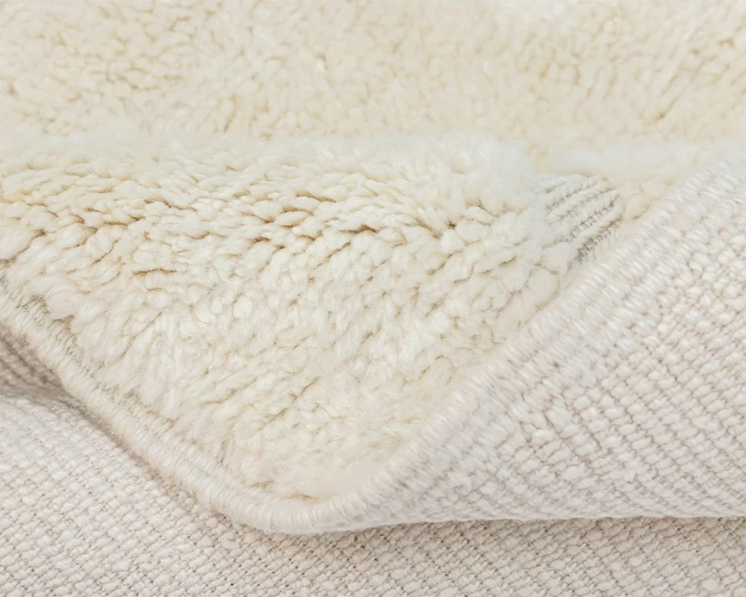 Close-up of a cream-colored, textured fleece rug with a soft, plush side and a woven underside.