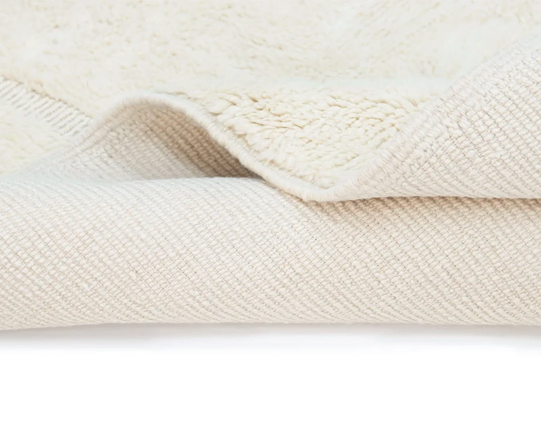 Close-up of a cream-colored textured rug with a visible soft, fuzzy underside folded over a woven surface.