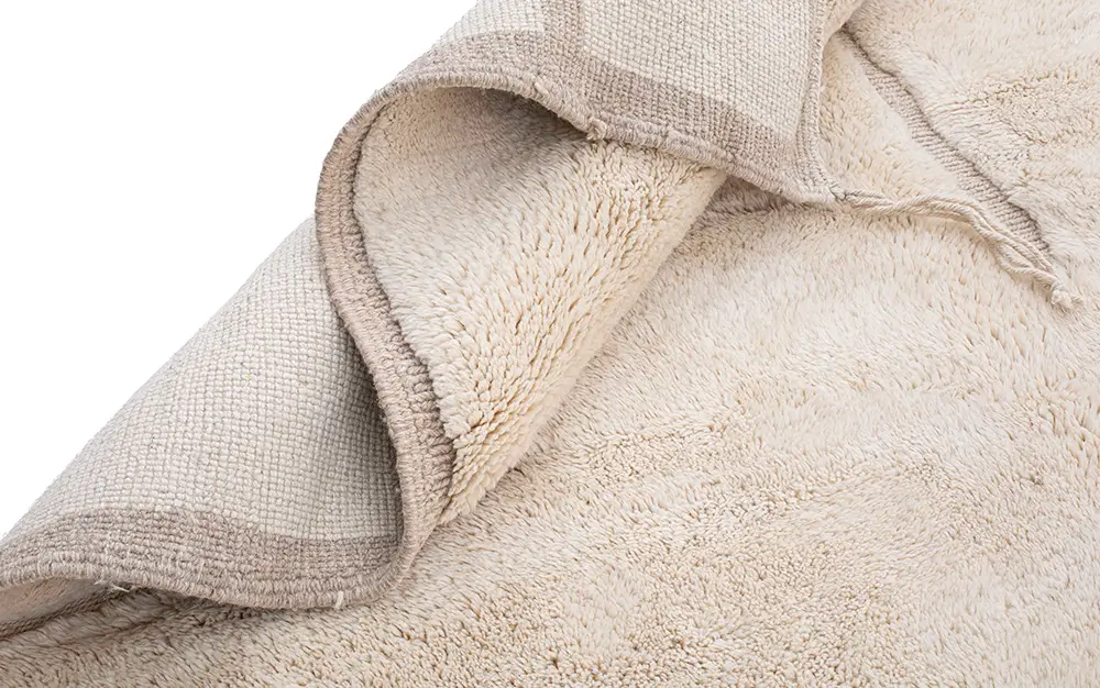 A close-up of an Authentic Moroccan Rug in light beige, with one corner flipped over to reveal the soft pile surface and hand-knotted woven backing.