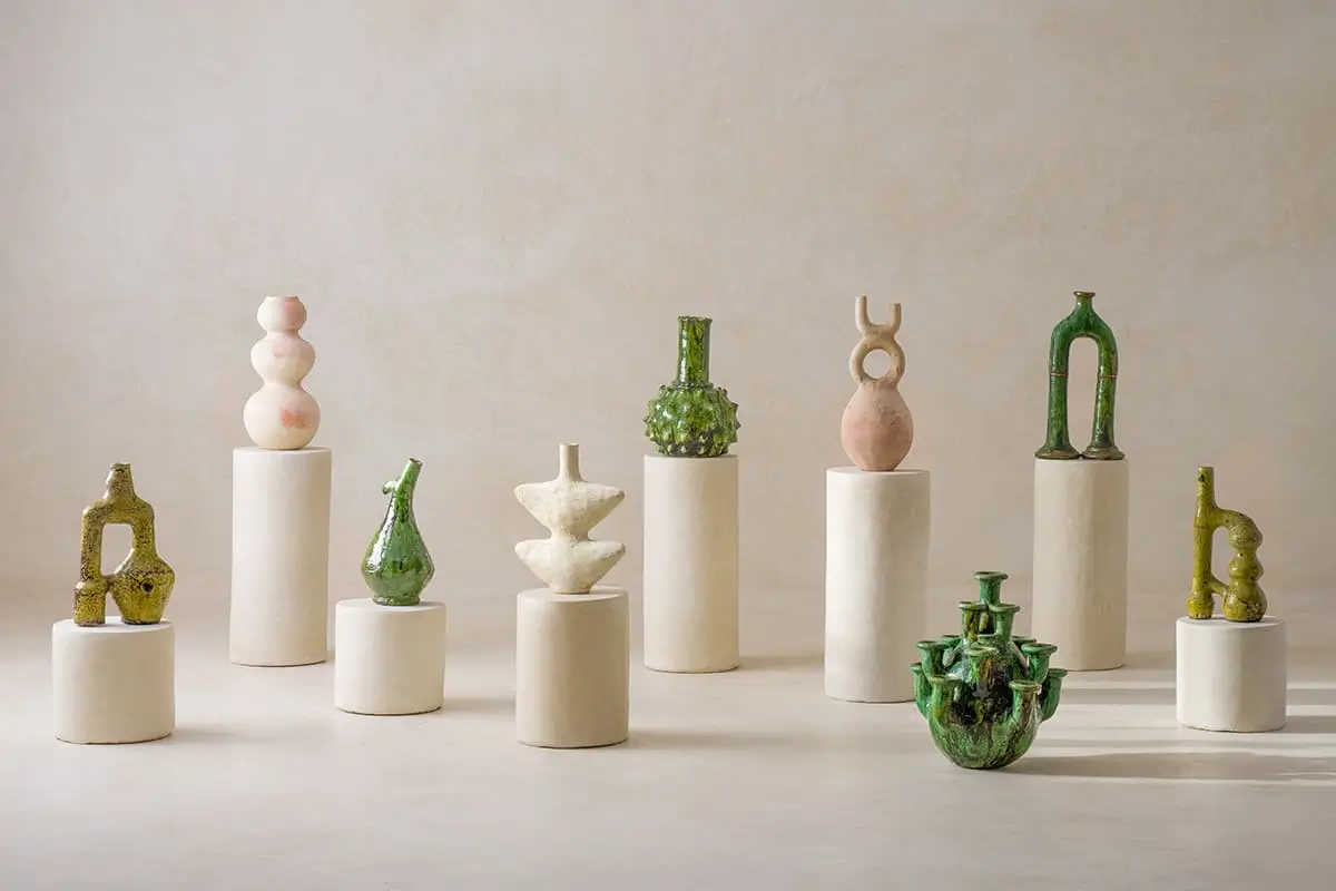 A collection of nine uniquely shaped Tamegroute Terracotta Pottery ceramic displayed on individual neutral pedestals arranged in a minimalist setting.