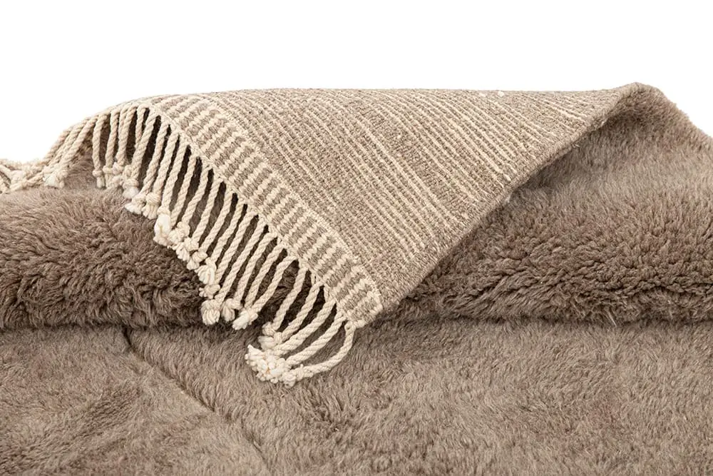 A beige, hand-knotted accent with a woven top and fringe detailing, placed over an authentic Moroccan rug for added texture and warmth.