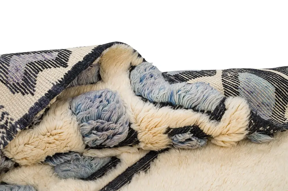 A close-up view of a folded, textured artisanal rug with patterned fabric on one side and soft, cream-colored fleece on the other.