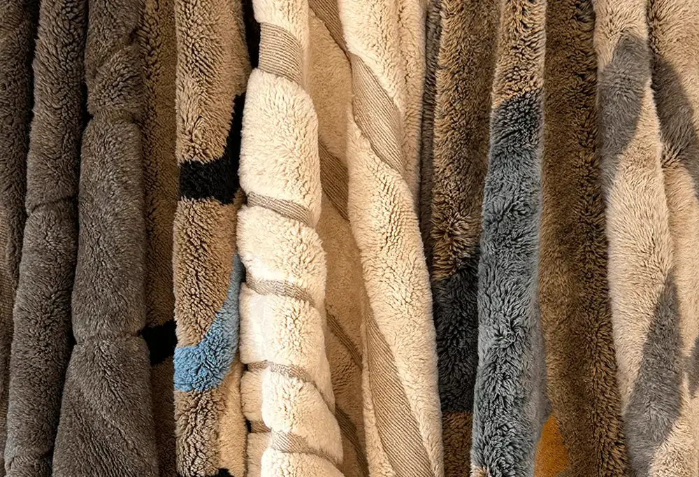 Several plush, textured textiles in shades of gray, beige, and cream hang closely together in vertical folds, reminiscent of the luxurious craftsmanship found in authentic Moroccan rugs.