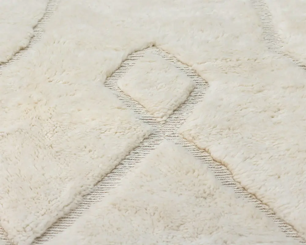 Close-up of an authentic Moroccan rug, hand-knotted with a cream-colored geometric diamond pattern and textured detail.