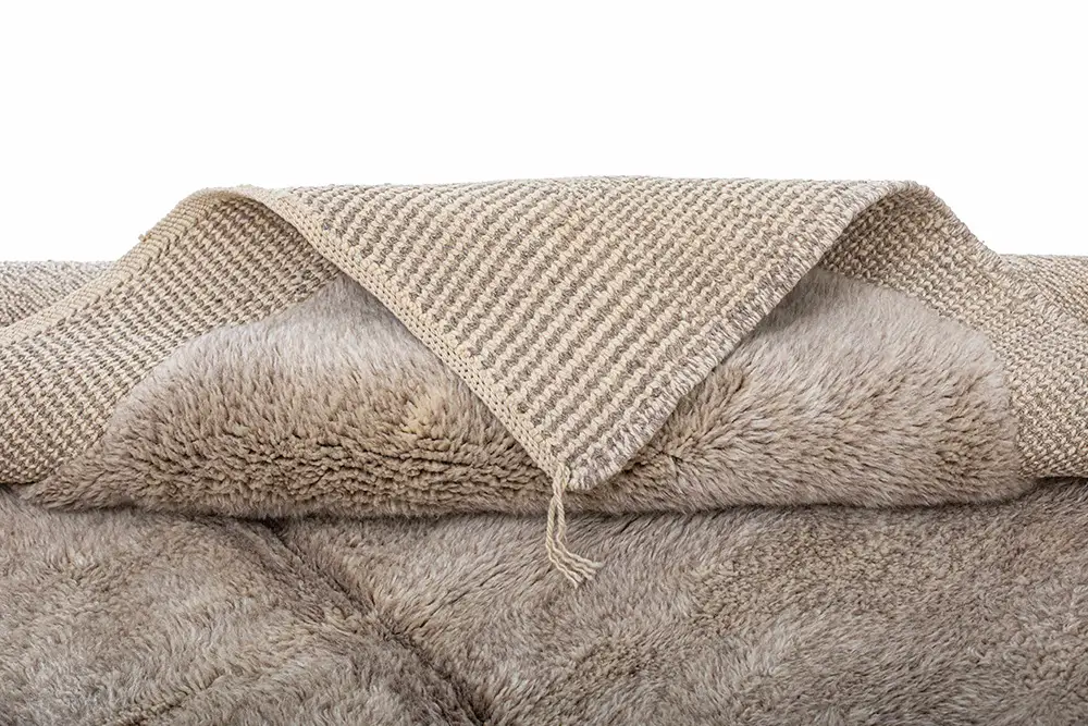 Close-up of a textured, hand-knotted rug with a woven pattern underneath, revealing its soft, luxurious surface.