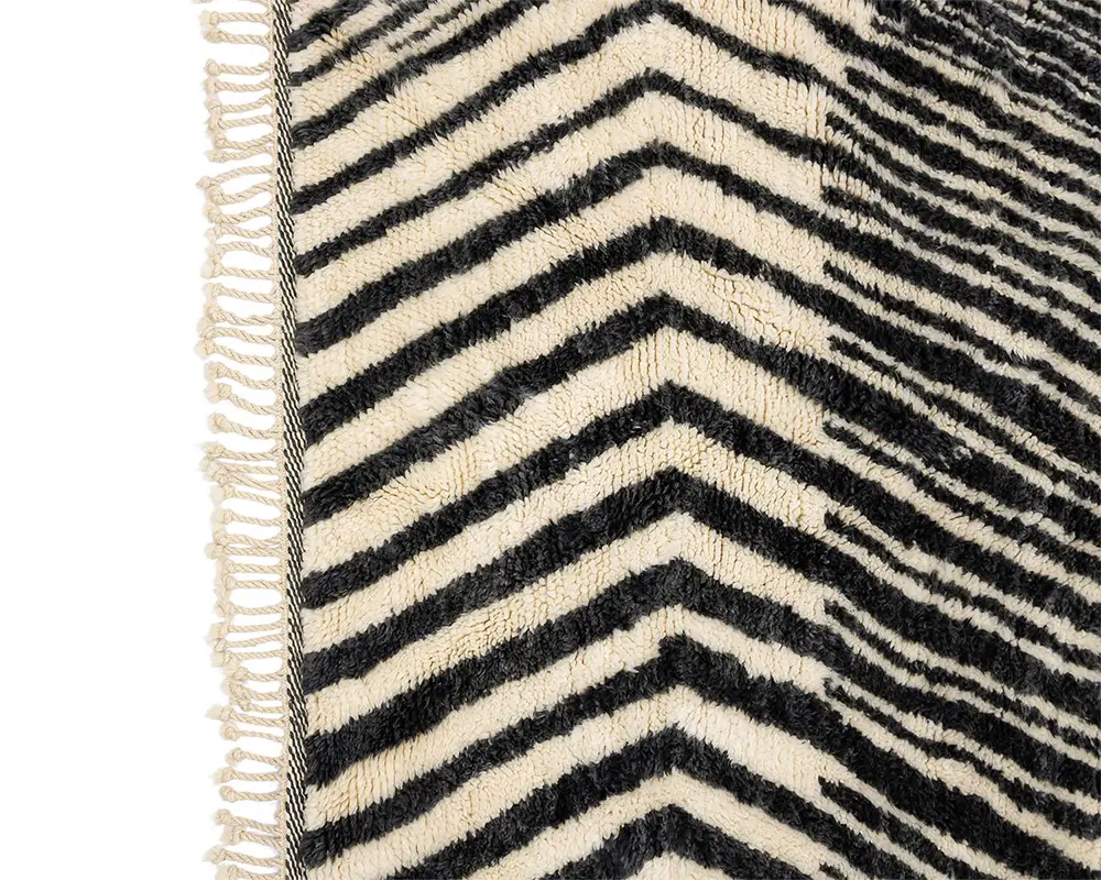 A close-up of a fabric featuring a black and white chevron pattern, highlighted by delicate fringe along the edge. This design adds a sophisticated touch to any decor.