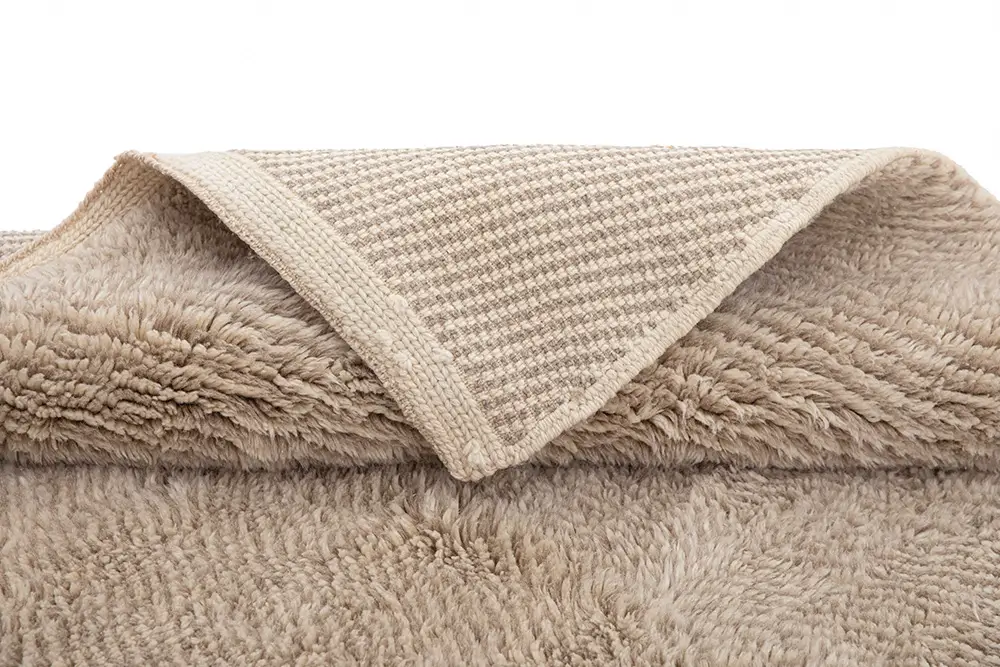 A close-up of a beige luxury rug with a folded corner, revealing its intricately woven underside, reminiscent of a traditional Moroccan design.