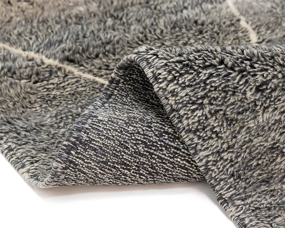 Close-up of a plush, folded grey and cream rug on a white background. The rug features a fluffy pile on one side and a woven underside, enhancing its cozy appeal.