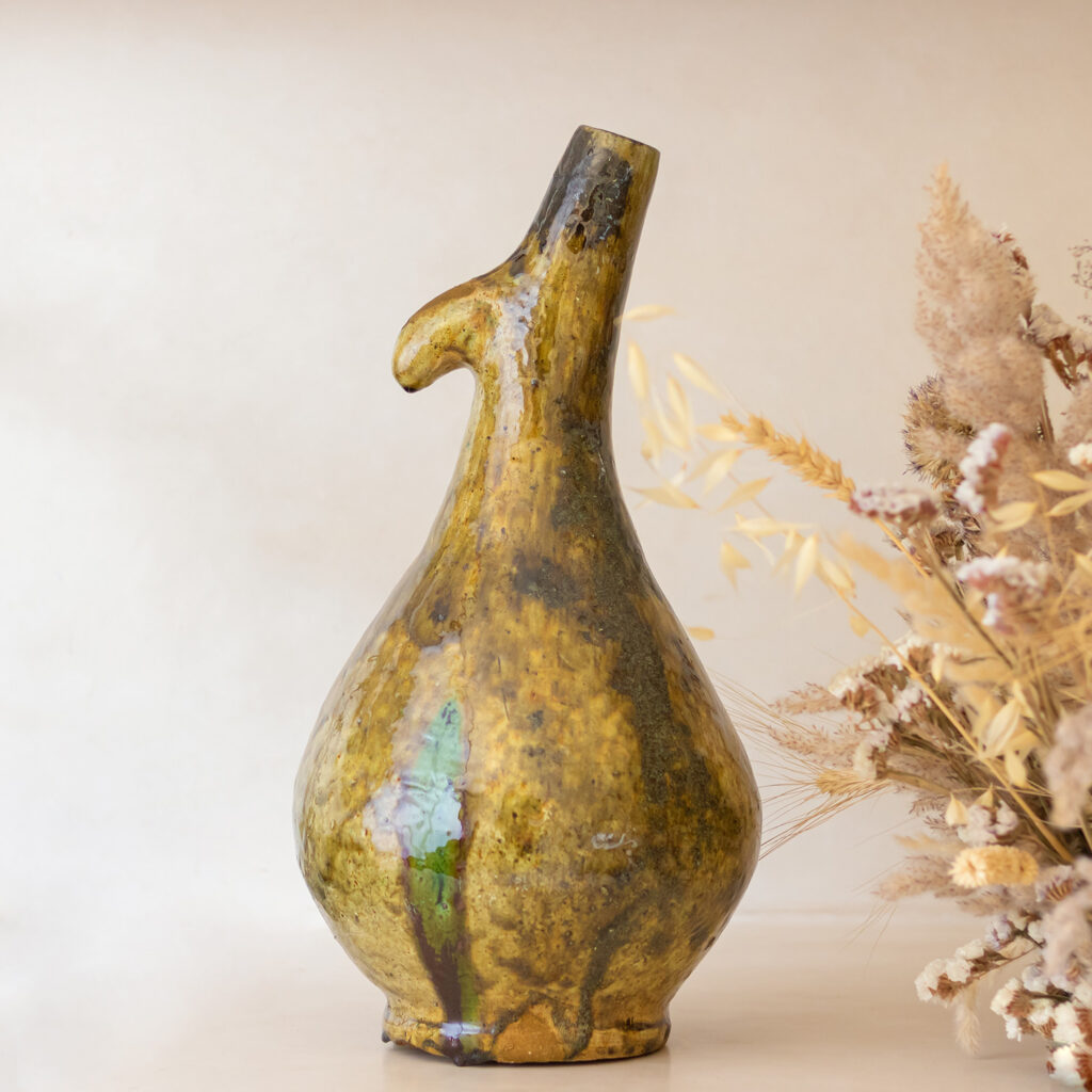 A ceramic vase with an abstract, irregular shape and earthy, metallic glaze elegantly stands beside dried grasses.