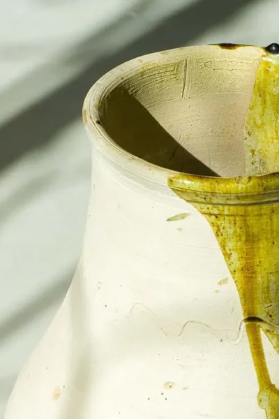 Ceramic vase with a dark green liquid dripping from the rim, casting shadows on a light surface.
